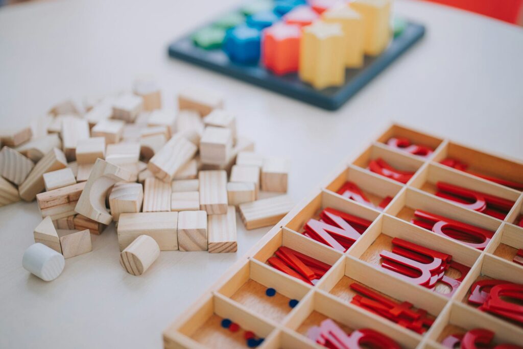 Montessori materials including wooden blocks, a shape sorting board, and the red moveable alphabet in a wooden tray